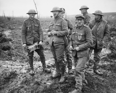 A group of six British soldiers during World War I stands in a muddy battlefield, wearing heavy wool uniforms and steel helmets, with a desolate, war-torn landscape in the background